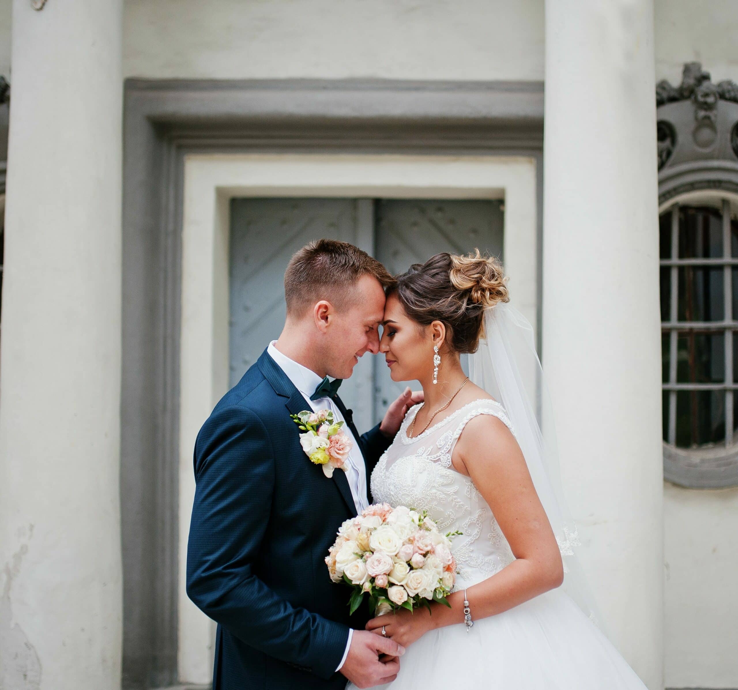 groom wearing navy suit standing with bride outside of white building