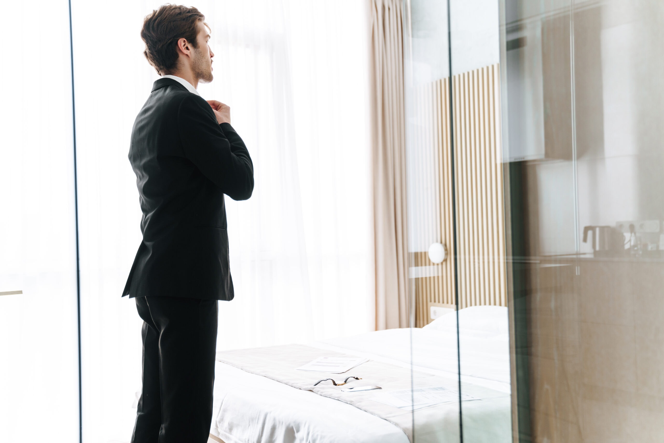 PhotoOfYoungBrunetteBusinessmanWearingBlackSuitStandingIn a man trying on his tuxedo rental at home